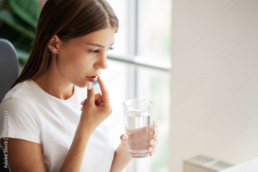 Young woman takes round pill with glass of water in hand Young woman takes round pill with glass of water in hand