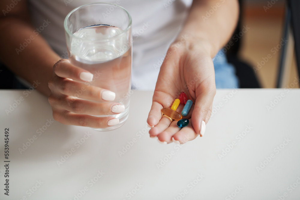 Young woman takes round pill with glass of water in hand Young woman takes round pill with glass of water in hand