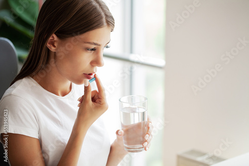 Young woman takes round pill with glass of water in hand