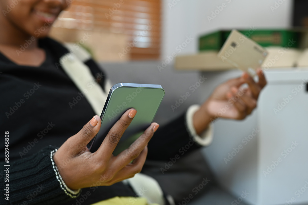 Cropped shot of smiling woman holding credit card, making payment on internet via mobile phone Cropped shot of smiling woman holding credit card, making payment on internet via mobile phone