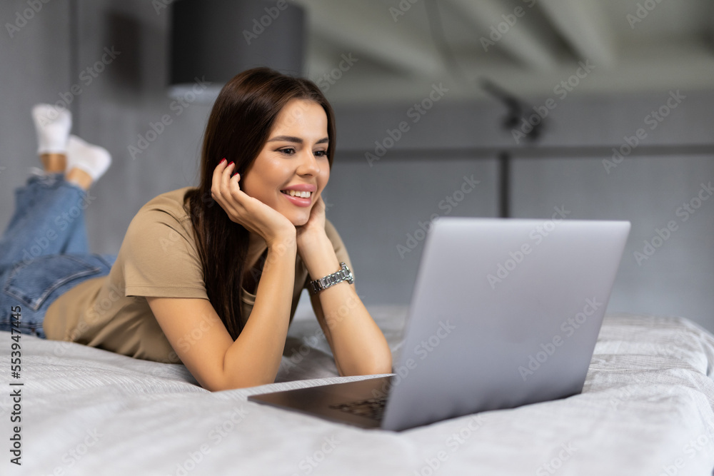 Beautiful woman lying in bed with a laptop at home Beautiful woman lying in bed with a laptop at home