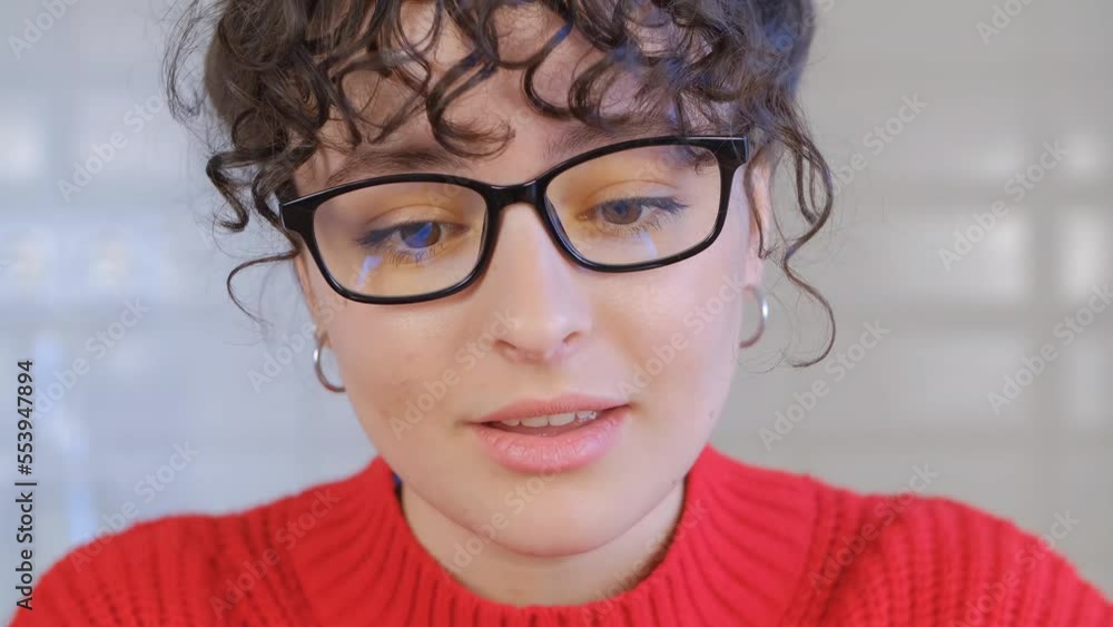 Beautiful Ukrainian girl talking on video call. Portrait of curly white woman in glasses speaking on web camera Beautiful Ukrainian girl talking on video call. Portrait of curly white woman in glasses speaking on web camera