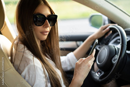successful business lady driving a car in sunglasses with a mobile phone in her hands.