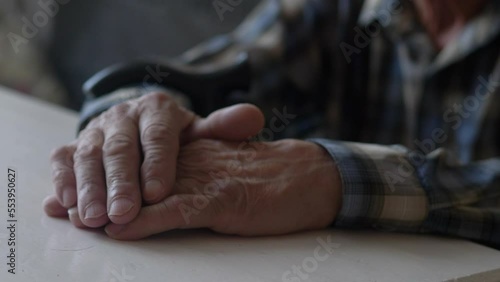close-up of the old man's hand on the table, selective focus. pensioner thinks with folded arms, elderly lonely people, real people are inside photo