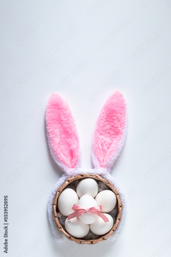Top view of basket with white Easter eggs and Easter bunny ears on white background, copy space for text