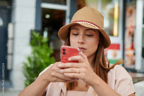 A beautiful Hispanic female in a hat sitting in a cafe with her cell phone on a sunny day