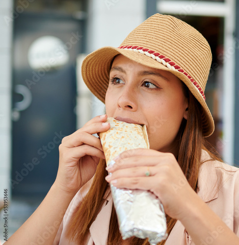 A closeup of a young female in a hat eating a kebab in a cafe on a sunny day
