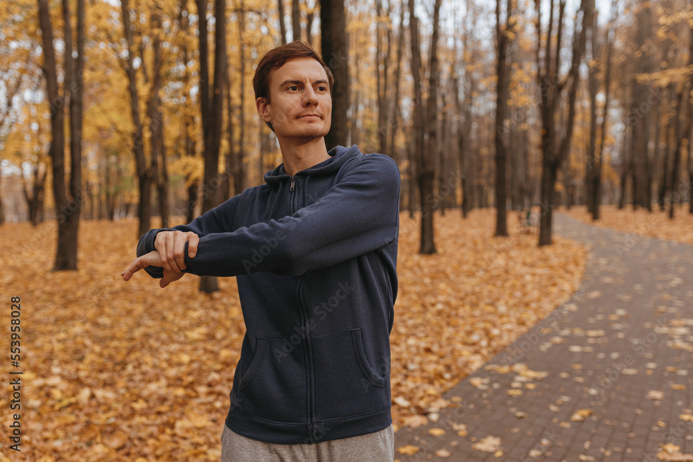 Athletic male jogger stretching and warming up while exercising during fitness training in autumn park Athletic male jogger stretching and warming up while exercising during fitness training in autumn park