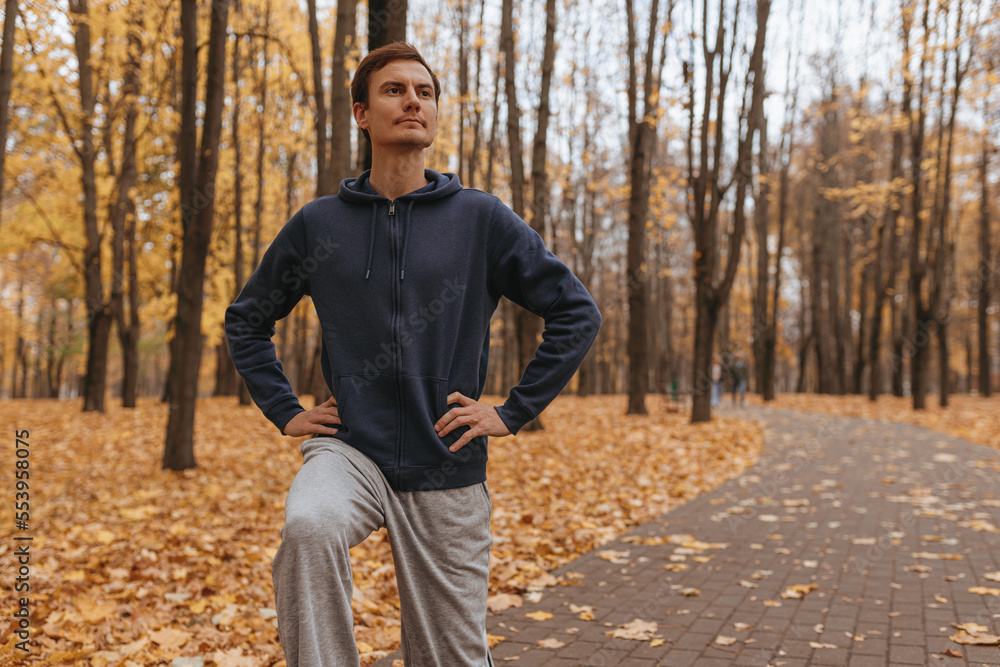 Male runner in sportswear warming up and doing exercise during training in autumn park 