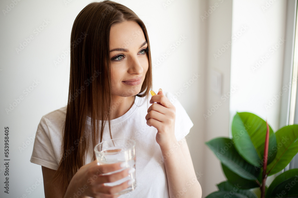 Woman taking vitamin pill with glass of fresh water indoors. Woman taking vitamin pill with glass of fresh water indoors.
