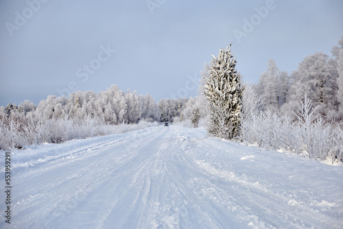 Winter landscape with snowy road and forest covered with hoar frost, selective focus