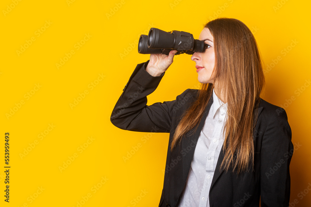 young business woman looking through binoculars on a yellow background young business woman looking through binoculars on a yellow background