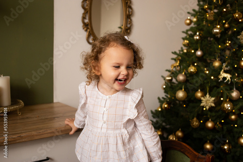 Little girl at home in kitchen Christmas tree. Happy girl playing near Christmas tree.