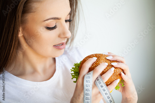 Beautiful Young Woman with burger and measuring tape while dieting