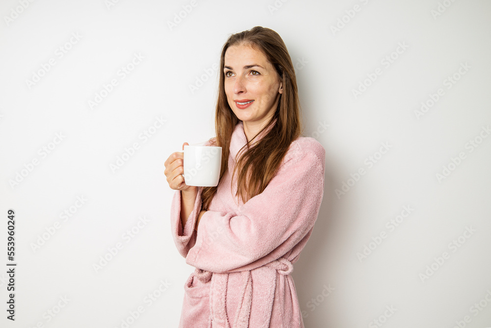 Smiling young woman in a bathrobe with a cup on a white background Smiling young woman in a bathrobe with a cup on a white background