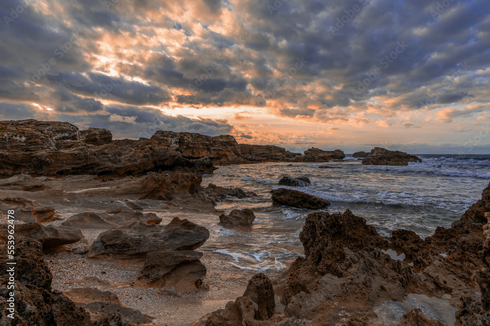 rocky cove and sandy beach under an expressive sunset sky on the rugged west coast of Sardinia