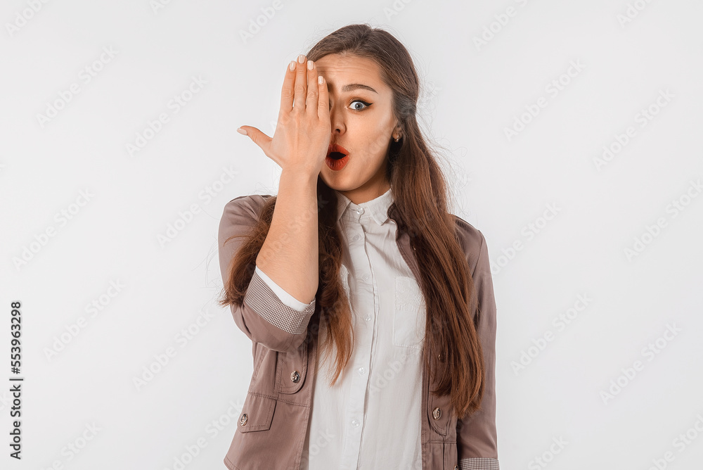 Excited girl covers half of face, looks with one eye at camera, holds palm on one side of face, standing over white background. Puzzled young woman standing against white studio background Excited girl covers half of face, looks with one eye at camera, holds palm on one side of face, standing over white background. Puzzled young woman standing against white studio background