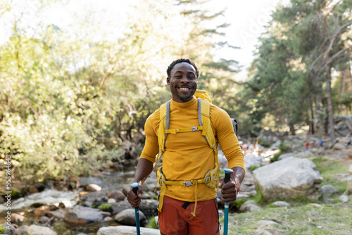 Cheerful middle age African American man trekking outdoors in the forest on a sunny day - Adventure lifestyle for people who love freedom and independence - Beautiful nature concept photo
