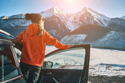 Woman traveling exploring, enjoying the view of the mountains, landscape, lifestyle concept winter vacation outdoors. Female standing near the car in sunny day, travel in the mountains, freedom
