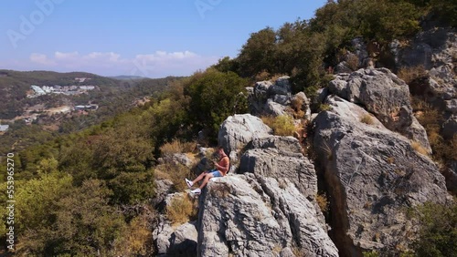 Young man sit on the rock of mountain, shooting himself aerial. Oludeniz beach background.  photo