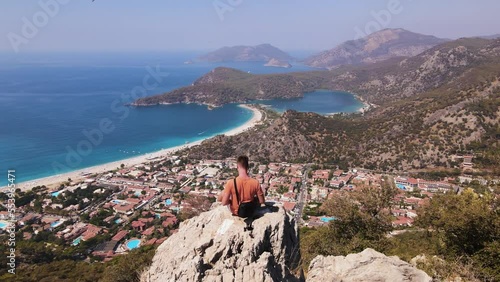 Aerial back view of young man sit on the rock of mountain, shooting himself aerial. Oludeniz beach background.  photo