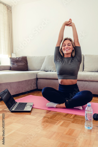 Young adult Caucasian woman sitting on the floor at home online yoga class practice watching instructions for training stretch relaxation.