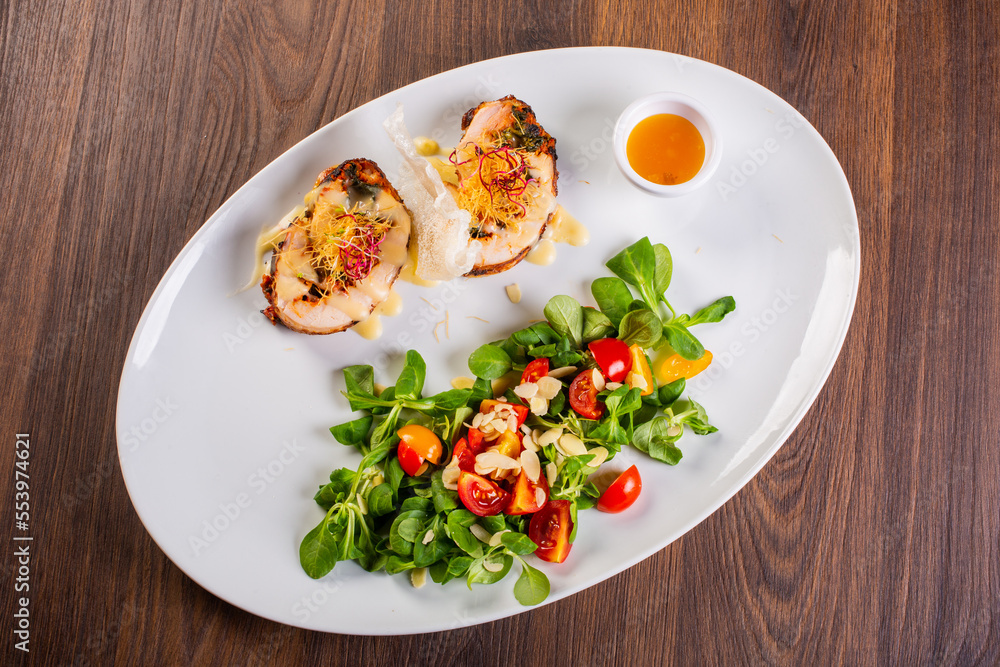 Involtini di pollo servito elegantemente in una braceria con contorno di rucola, pomodori gialli e rossi e scagli di formaggio accompagnati da una salsa agrodolce Involtini di pollo servito elegantemente in una braceria con contorno di rucola, pomodori gialli e rossi e scagli di formaggio accompagnati da una salsa agrodolce