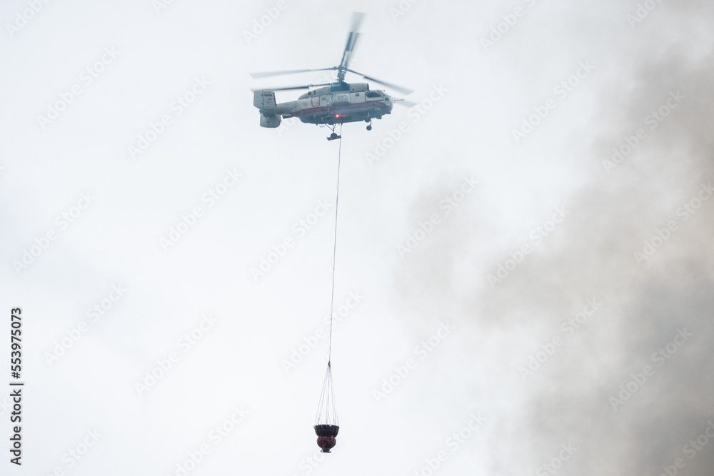 A fire helicopter carries a container of water to extinguish a fire in a production building A fire helicopter carries a container of water to extinguish a fire in a production building