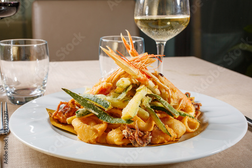 Frittura mista di pesce e verdure servita in un ristorante elegante accompagnata da un calice di vino bianco