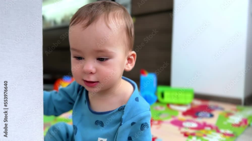 Cute little boy sits on the floor playing with his toys scattered by the room. Mom is busy with her things to do at backdrop in blur. Cute little boy sits on the floor playing with his toys scattered by the room. Mom is busy with her things to do at backdrop in blur.