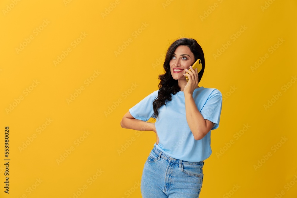 Woman blogger with a phone in her hands in a blue t-shirt and jeans on a yellow background smile signs gestures symbols, online communication and video call, copy space, free background Woman blogger with a phone in her hands in a blue t-shirt and jeans on a yellow background smile signs gestures symbols, online communication and video call, copy space, free background