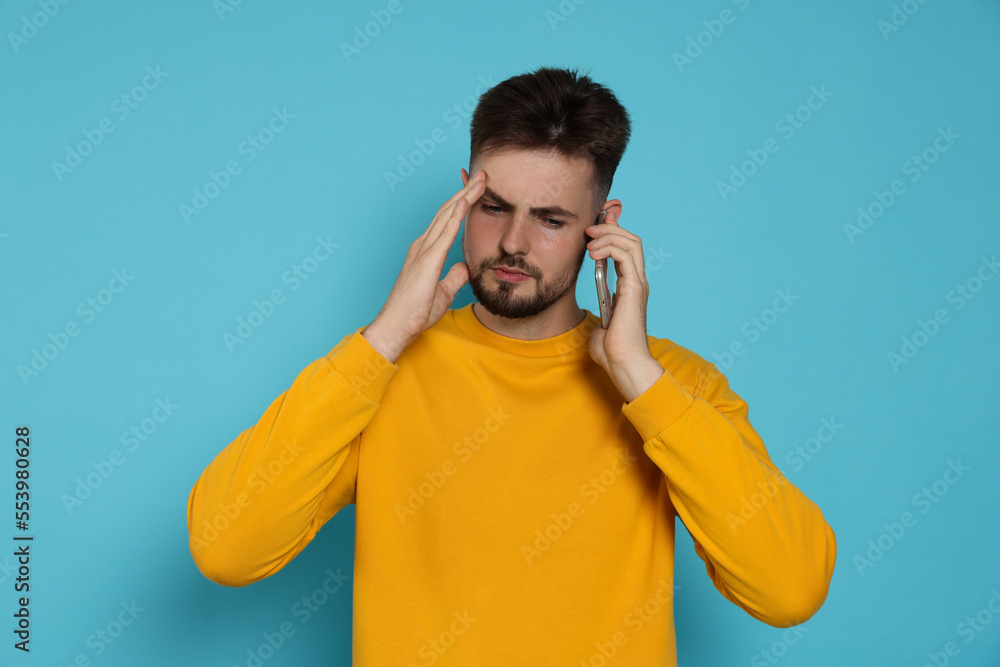 Stressed man in yellow sweatshirt talking on phone against light blue background Stressed man in yellow sweatshirt talking on phone against light blue background