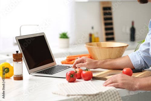 Man making dinner while watching online cooking course via laptop in kitchen  closeup