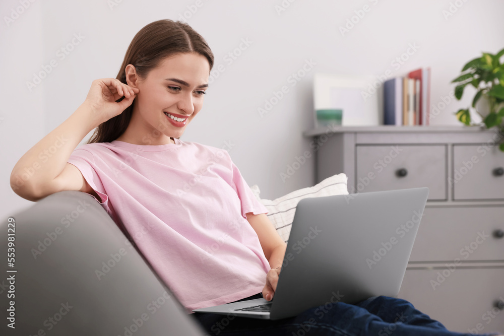 Fototapeta premium Happy young woman with laptop on sofa at home