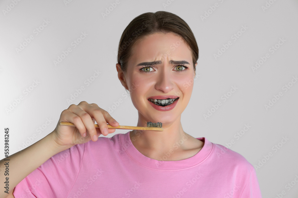 Young woman brushing teeth with charcoal toothpaste on light background Young woman brushing teeth with charcoal toothpaste on light background