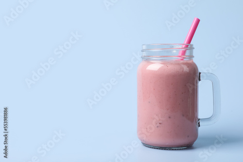 Mason jar with delicious berry smoothie on light blue background. Space for text
