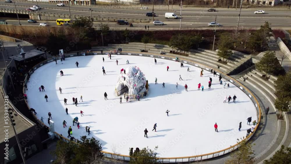 Ice skating rink in open air in city on sunny winter day. Many people ...