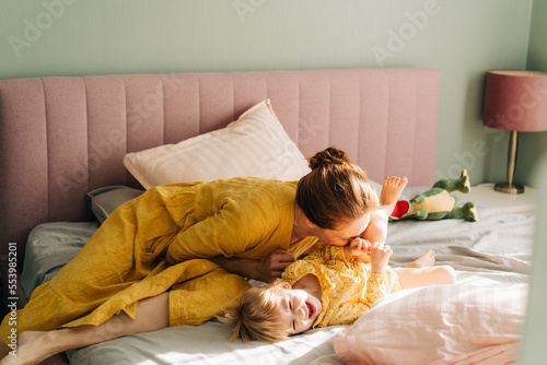 Mom tickles and kisses her little laughing daughter in the morning on the bed in the apartment. photo