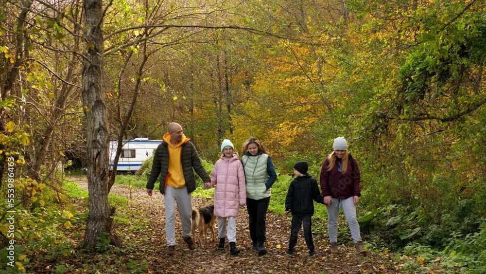 A big happy family with three children and a big dog are walking along a path in the autumn forest. A big happy family with three children and a big dog are walking along a path in the autumn forest.