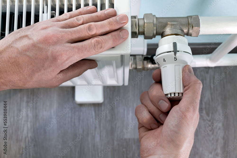 Man regulates the heat supply of a radiator with a thermostat knob. And ...