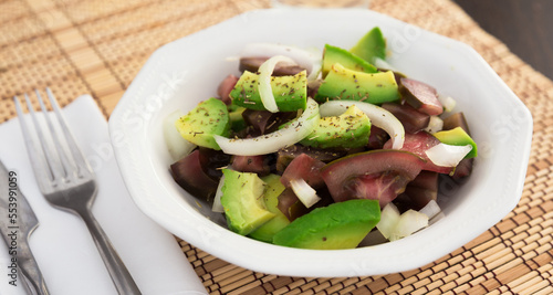 salad of black tomatoes, avocado and onions in white ceramic bowl