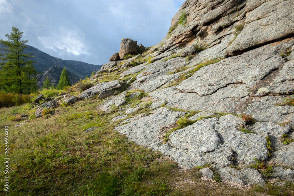 Rocky foothill with the clouds and blue sky in the background. Rock mountain in Mongolia on a cloudy day. Rocky foothill with the clouds and blue sky in the background. Rock mountain in Mongolia on a cloudy day.