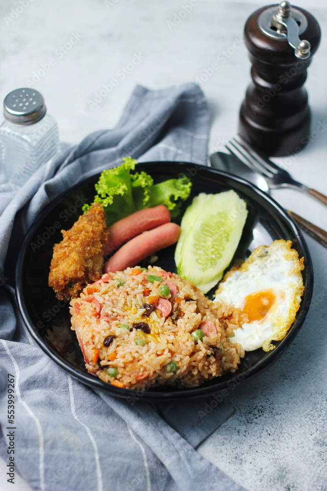 Fried rice with peanuts, carrots, raisins Served with fried chicken, fried egg, and fried sausage. Served on a black plate on a white table in a restaurant. Fried rice with peanuts, carrots, raisins Served with fried chicken, fried egg, and fried sausage. Served on a black plate on a white table in a restaurant.