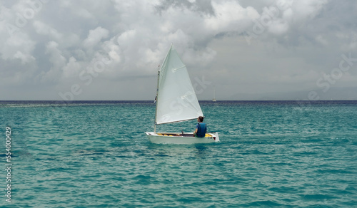 Lonely sailor on training sailing pram optimist education boat in the sea in Greece, water background and cloudy sky photo