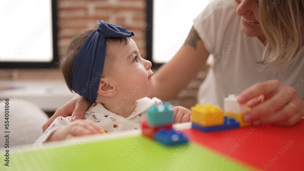 Woman and toddler playing with construction blocks sitting on table at kindergarten Woman and toddler playing with construction blocks sitting on table at kindergarten