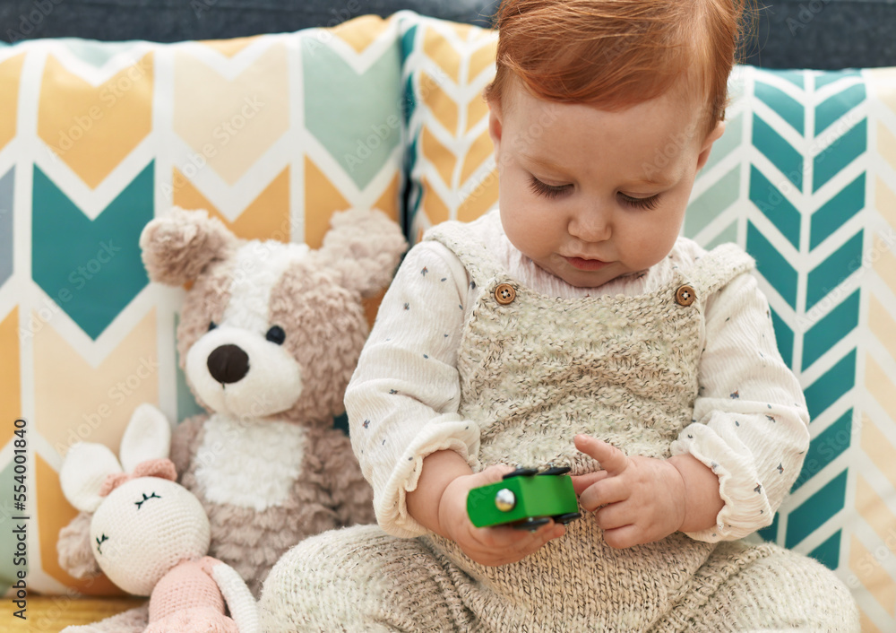 Adorable redhead toddler playing with car toy sitting on sofa at home Adorable redhead toddler playing with car toy sitting on sofa at home