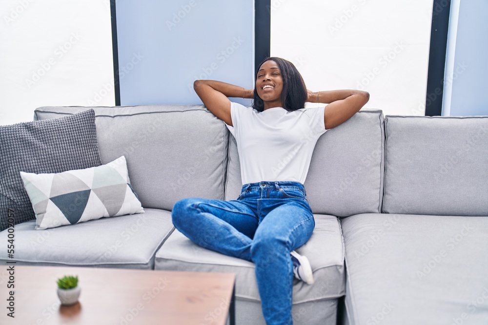 Young african american woman relaxed with hands on head sitting on sofa at home