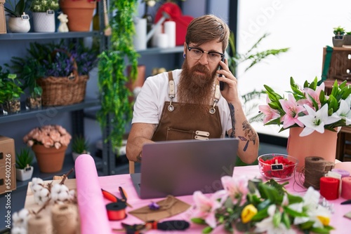 Young redhead man florist talking on smartphone using laptop at flower shop © Krakenimages.com