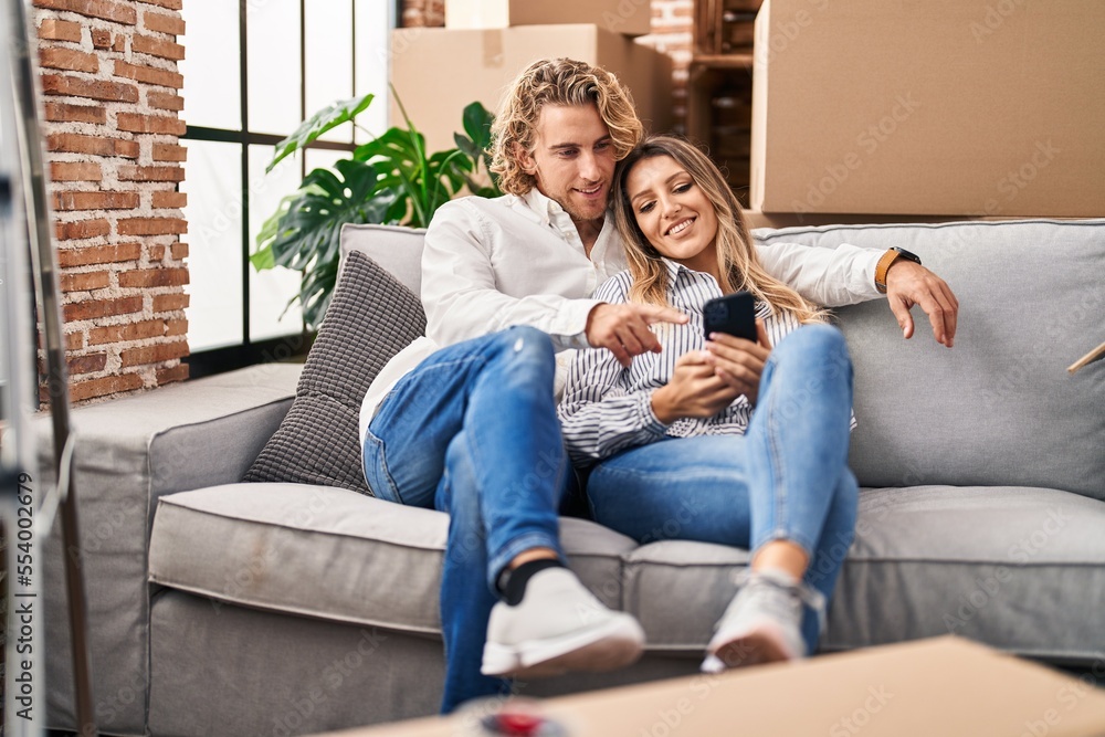 Man and woman couple using smartphone sitting on sofa at new home