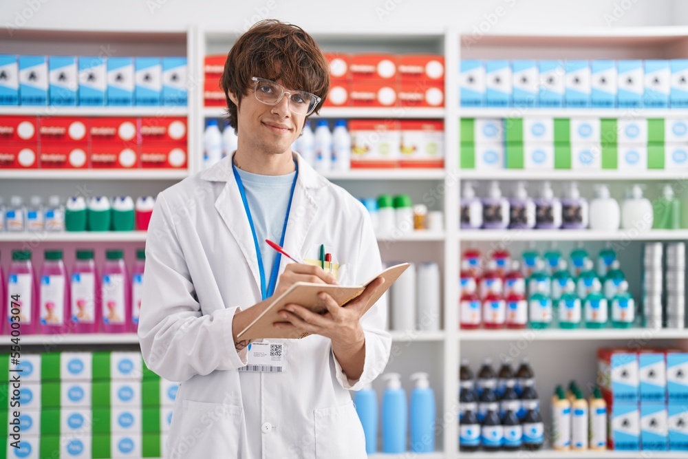Young blond man pharmacist writing on notebook at pharmacy Young blond man pharmacist writing on notebook at pharmacy